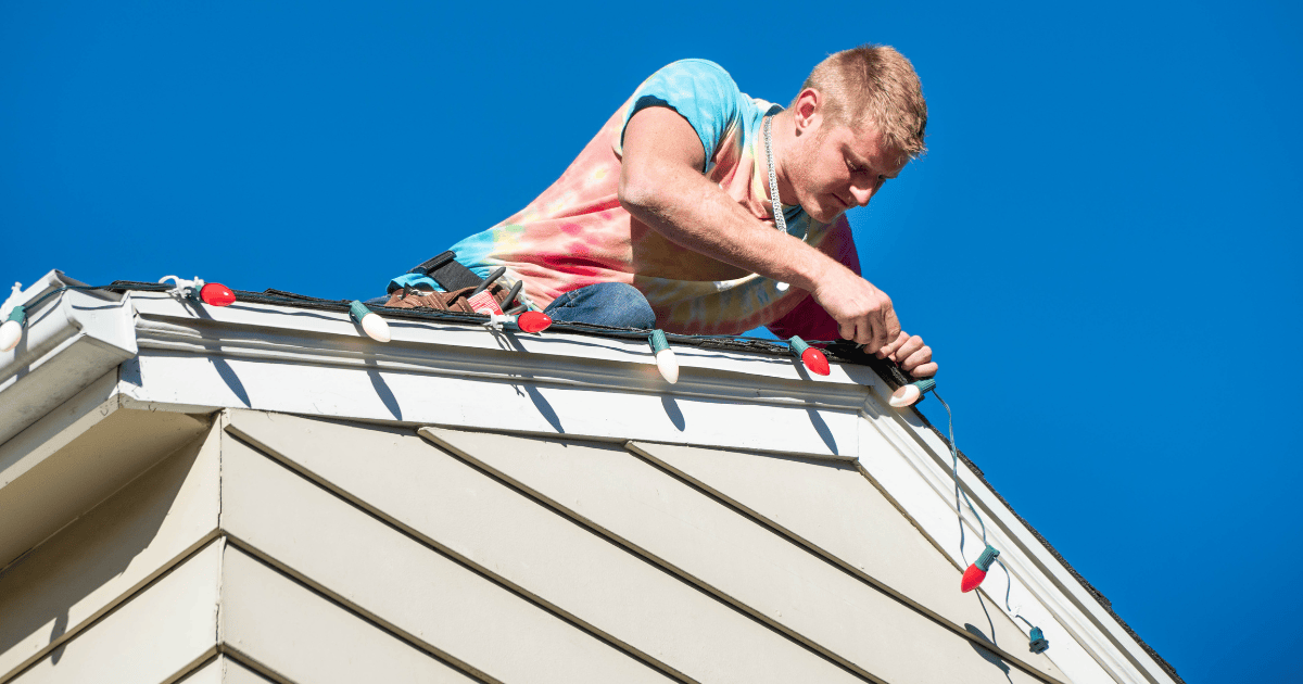 a man hanging holiday lights on a roof