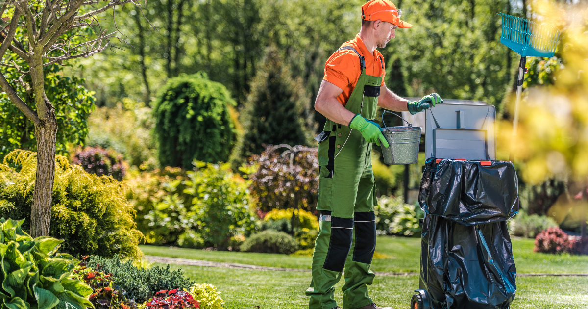 a man wheeling a large garbage can cleaning up yard waste